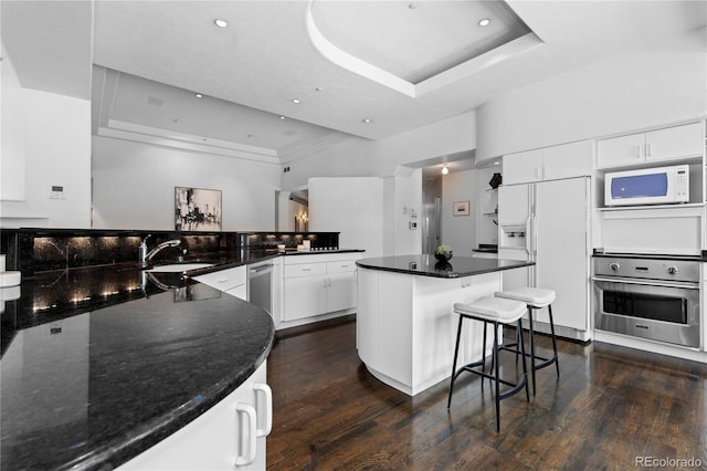 kitchen featuring a tray ceiling, dark wood-style flooring, a sink, and white appliances
