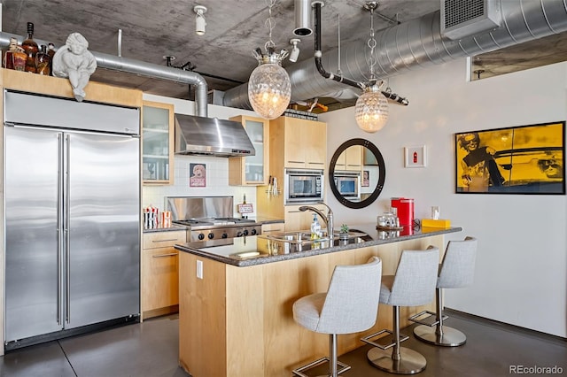 kitchen featuring sink, built in appliances, a kitchen breakfast bar, decorative backsplash, and wall chimney range hood