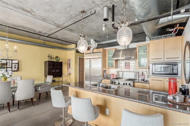 2100 16th St Unit 606, Denver, CO 80202 - kitchen featuring a sink, wall chimney range hood, built in appliances, a kitchen breakfast bar, and glass insert cabinets
