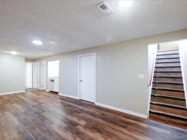 below grade area featuring a textured ceiling, baseboards, visible vents, stairs, and wood finished floors