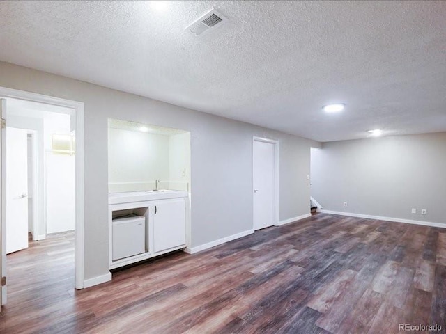 below grade area featuring a textured ceiling, visible vents, baseboards, and dark wood-style floors