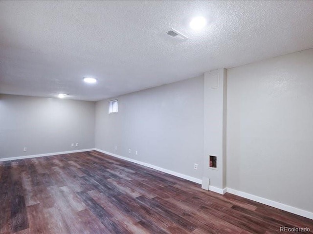 below grade area with a textured ceiling, baseboards, visible vents, and wood finished floors