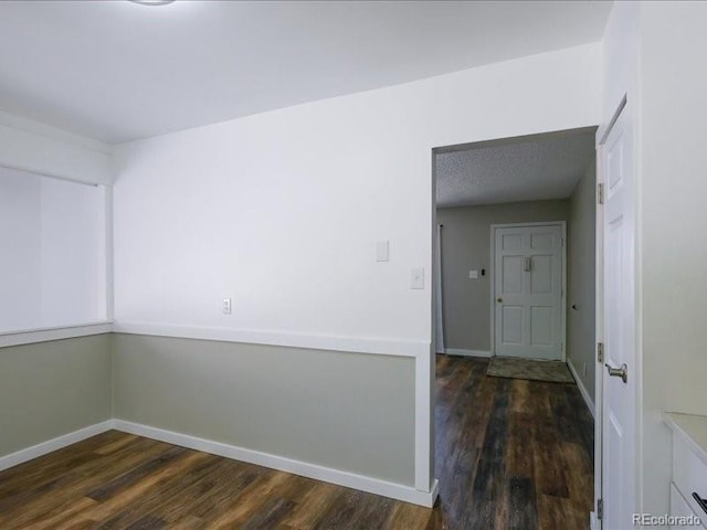spare room featuring dark wood-style flooring and baseboards