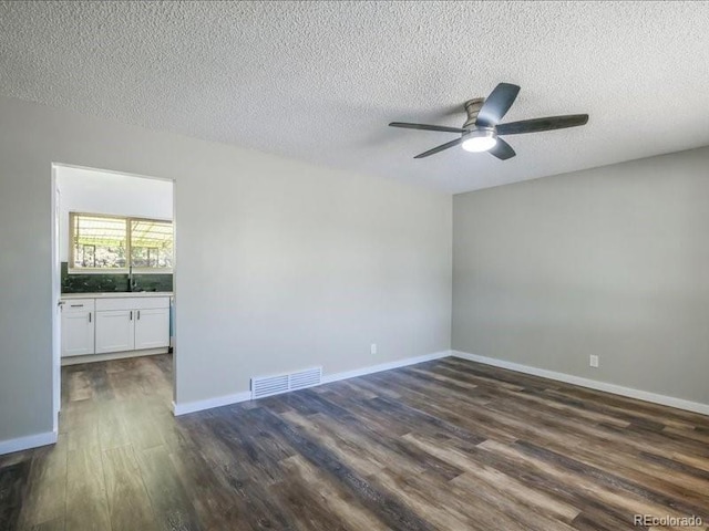 spare room featuring a textured ceiling, visible vents, dark wood finished floors, ceiling fan, and baseboards