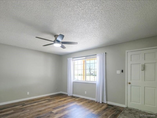 spare room featuring a ceiling fan, dark wood finished floors, visible vents, and a textured ceiling