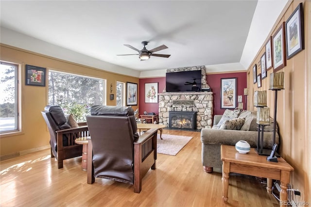 living room with a stone fireplace, ceiling fan, and light hardwood / wood-style flooring