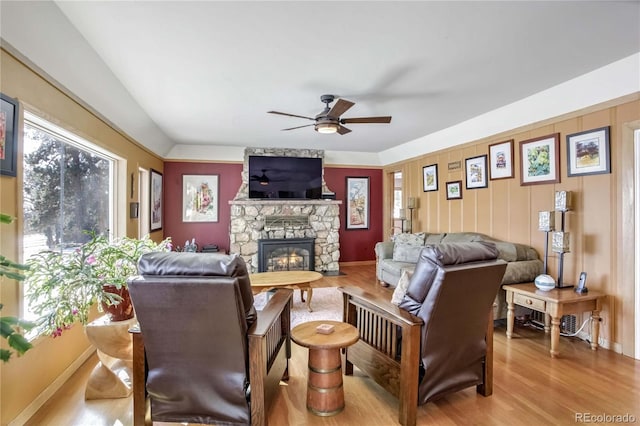 living area featuring baseboards, ceiling fan, a fireplace, and light wood-style flooring