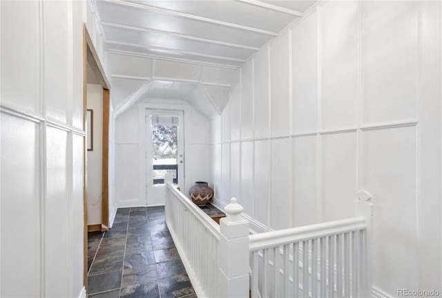 corridor with baseboards, stone tile floors, a decorative wall, and an upstairs landing