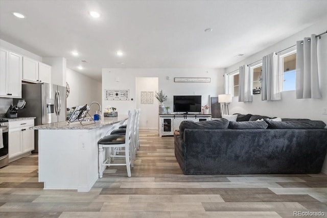 kitchen featuring light stone counters, recessed lighting, open floor plan, white cabinetry, and light wood-type flooring