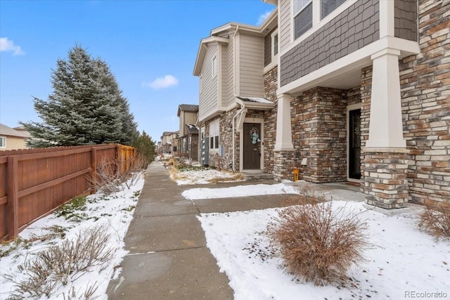 view of snowy exterior featuring stone siding and fence