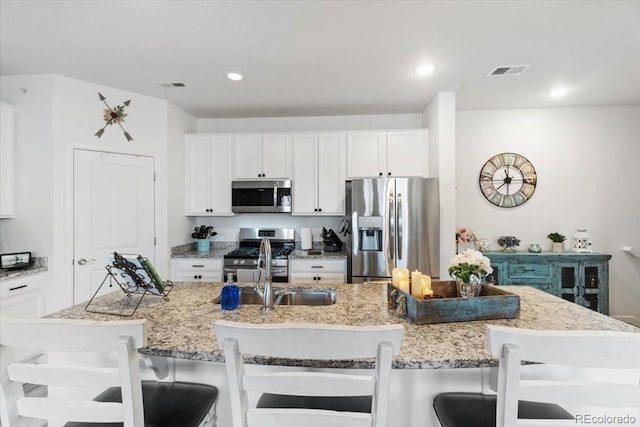 kitchen with stainless steel appliances, a breakfast bar, visible vents, and light stone counters