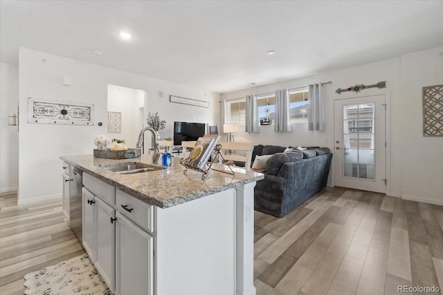 kitchen featuring stainless steel dishwasher, light wood-style flooring, open floor plan, and a sink