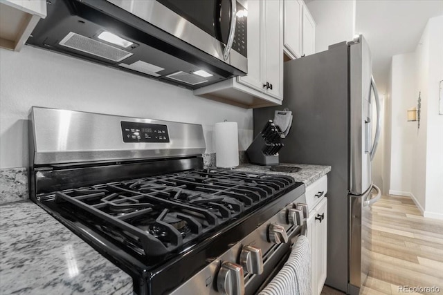 kitchen with baseboards, light stone counters, stainless steel appliances, light wood-style floors, and white cabinetry