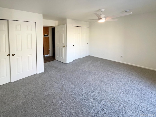 unfurnished bedroom featuring dark carpet, ceiling fan, and multiple closets