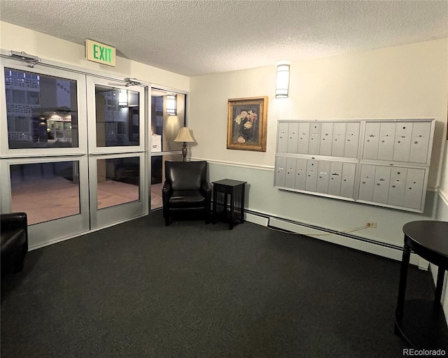 sitting room with a textured ceiling, dark colored carpet, a baseboard radiator, and mail area