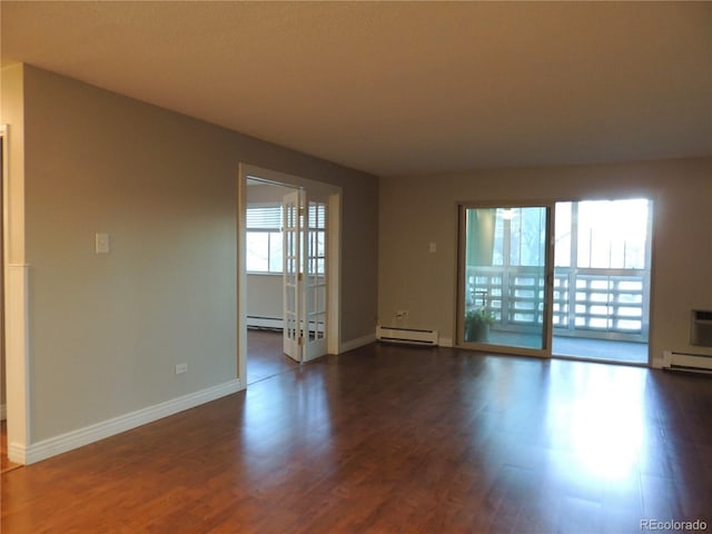 spare room with a baseboard heating unit, dark wood finished floors, and baseboards