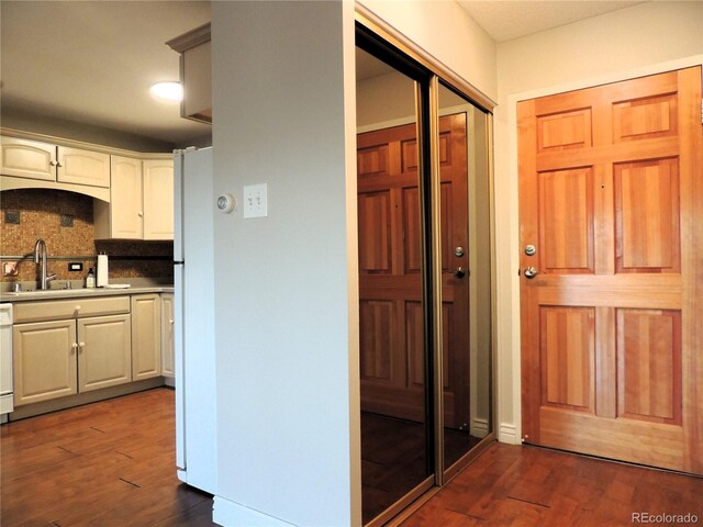 kitchen featuring dishwashing machine, dark wood-style floors, freestanding refrigerator, a sink, and backsplash