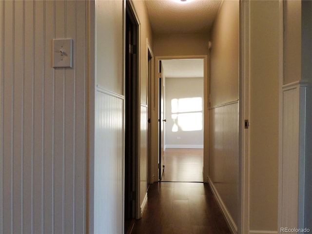 hallway featuring a wainscoted wall and dark wood-style flooring