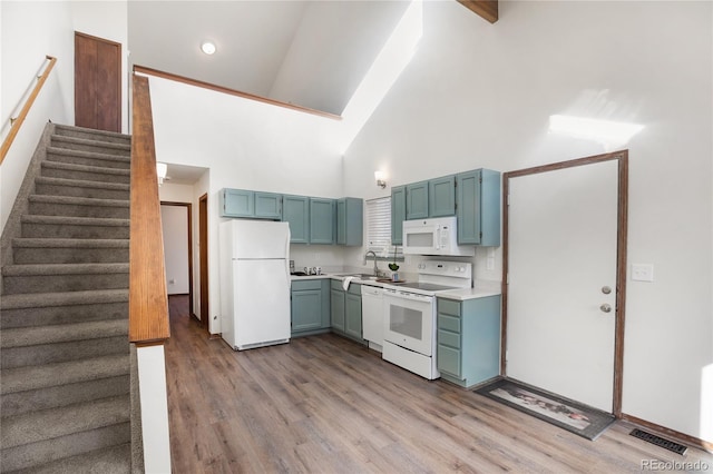 kitchen with high vaulted ceiling, light wood-style flooring, a sink, white appliances, and light countertops