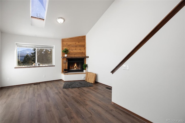 unfurnished living room with wood finished floors, visible vents, baseboards, a skylight, and a warm lit fireplace