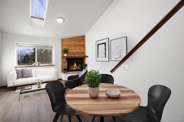 dining space featuring a warm lit fireplace, a skylight, and wood finished floors