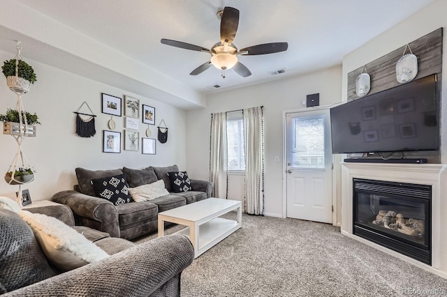 carpeted living room with a ceiling fan, a glass covered fireplace, visible vents, and baseboards