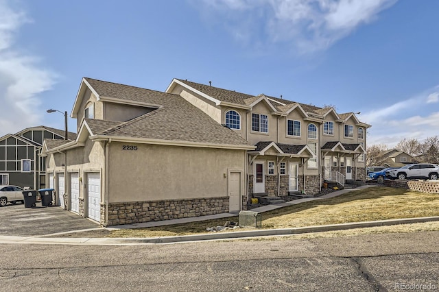 view of front facade featuring aphalt driveway, an attached garage, a shingled roof, stone siding, and stucco siding