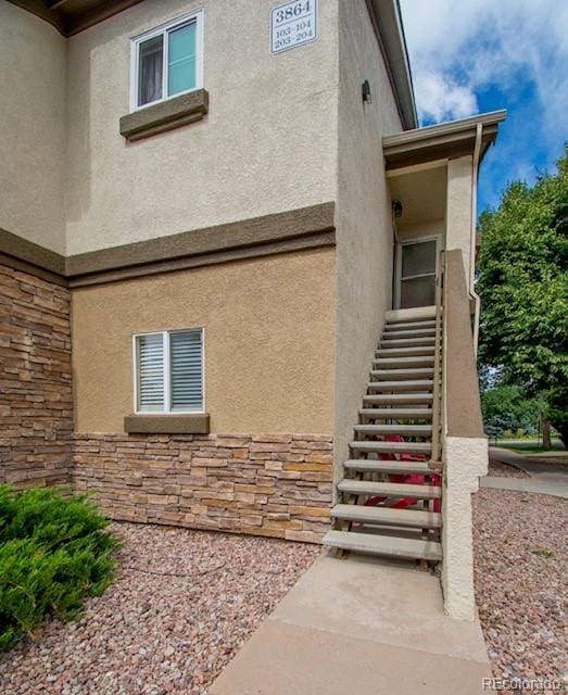 view of home's exterior with stairs, stone siding, and stucco siding