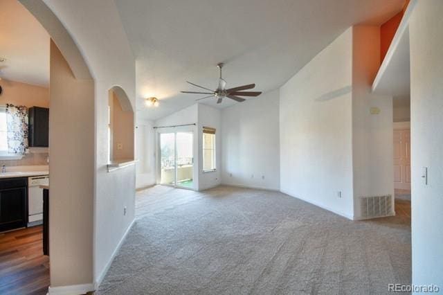 carpeted spare room featuring arched walkways, vaulted ceiling, visible vents, and a ceiling fan