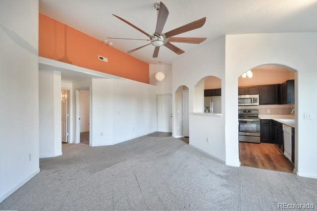 unfurnished living room with light colored carpet, visible vents, a sink, ceiling fan, and high vaulted ceiling