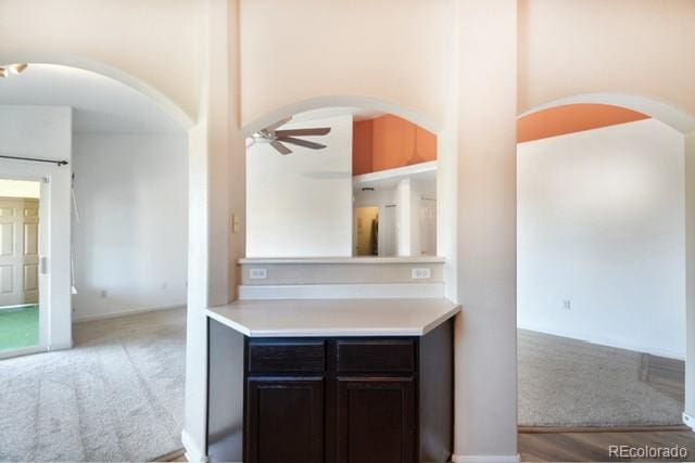 kitchen with a ceiling fan, light countertops, light carpet, and arched walkways