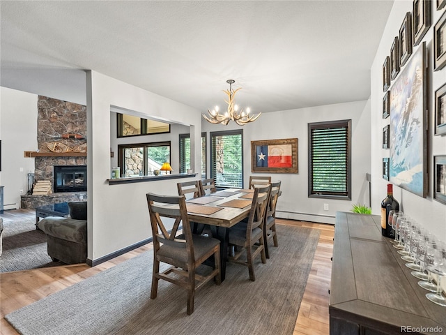 dining space with light wood-style flooring, baseboard heating, a notable chandelier, and a stone fireplace