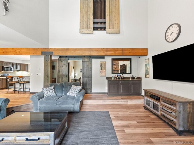 living area with light wood-style floors, a towering ceiling, and a barn door