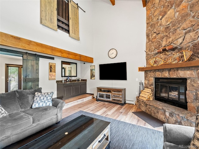 living room with a barn door, wood finished floors, a high ceiling, baseboard heating, and a fireplace