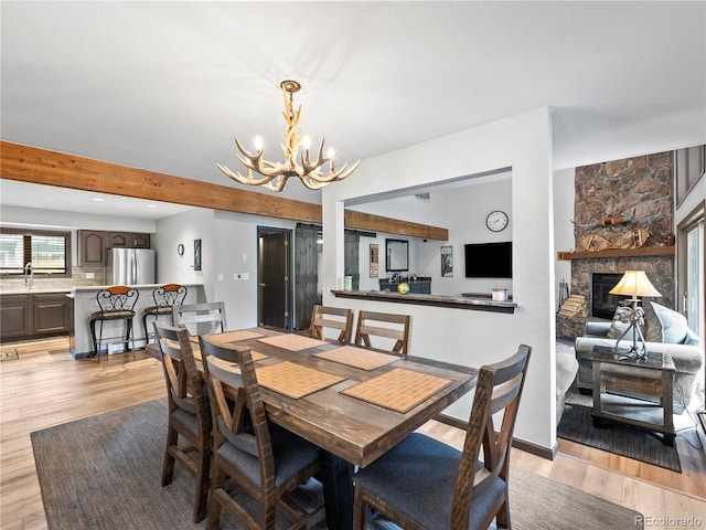 dining space featuring beamed ceiling, light wood-type flooring, a fireplace, and a notable chandelier