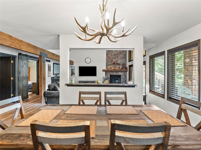 dining area featuring a barn door, a fireplace, wood finished floors, and an inviting chandelier