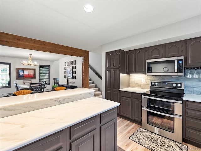 kitchen with light wood finished floors, decorative backsplash, appliances with stainless steel finishes, light countertops, and a notable chandelier