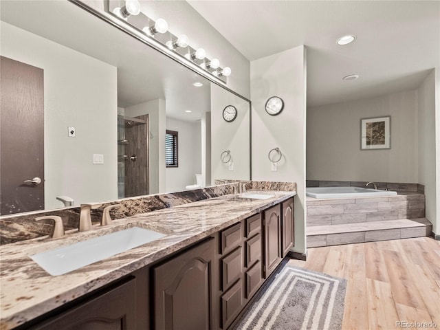 full bathroom with double vanity, a stall shower, wood finished floors, a garden tub, and a sink