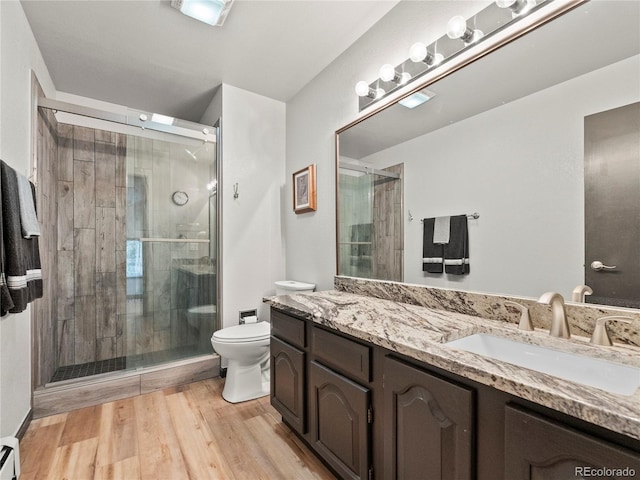 bathroom featuring a baseboard radiator, toilet, vanity, a shower stall, and wood finished floors