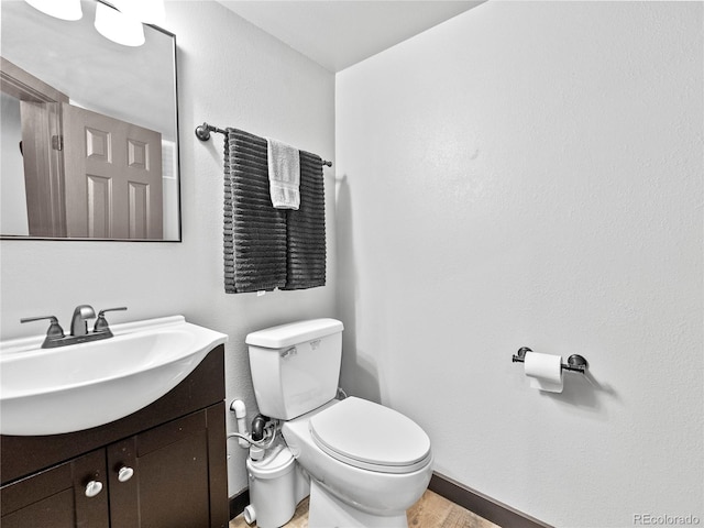 half bathroom featuring baseboards, vanity, toilet, and wood finished floors