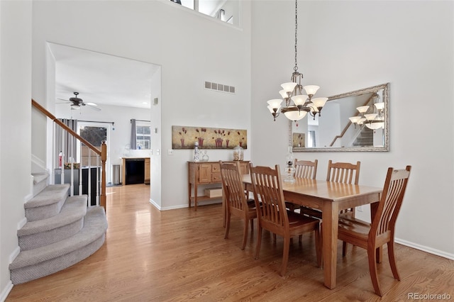 dining room featuring ceiling fan with notable chandelier, hardwood / wood-style flooring, and a towering ceiling