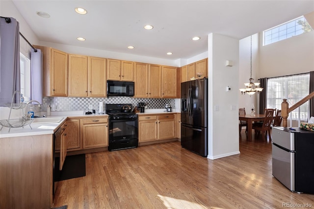 kitchen featuring black appliances, light hardwood / wood-style floors, pendant lighting, sink, and tasteful backsplash