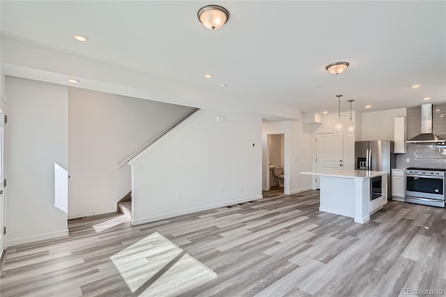 kitchen with wall chimney exhaust hood, stainless steel appliances, tasteful backsplash, decorative light fixtures, and a kitchen island