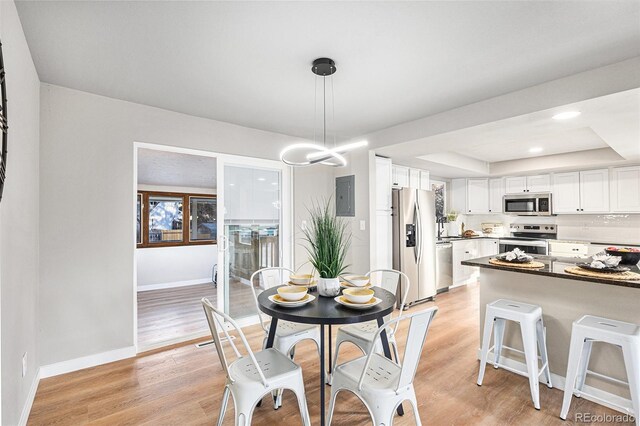 dining space with light wood-type flooring, electric panel, and a raised ceiling