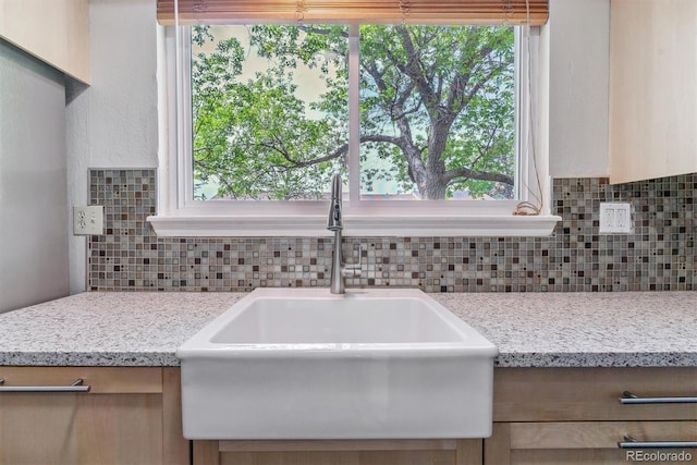 kitchen with a sink, backsplash, light stone countertops, and healthy amount of natural light