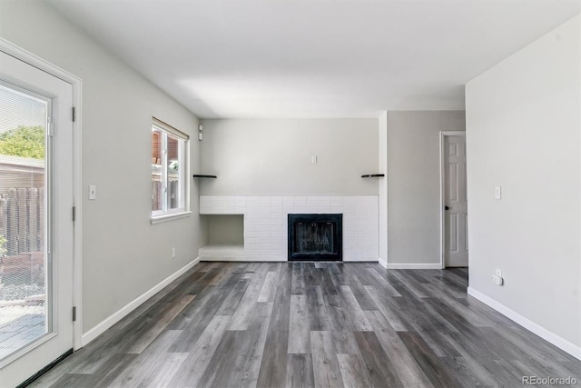 unfurnished living room with dark wood finished floors, a brick fireplace, and baseboards