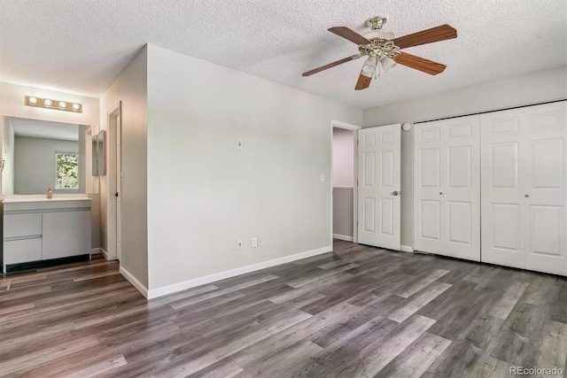 unfurnished bedroom with wood finished floors, a textured ceiling, a sink, a closet, and baseboards