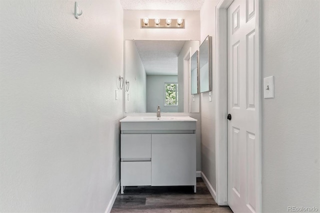 bathroom with wood finished floors, vanity, a textured ceiling, and baseboards