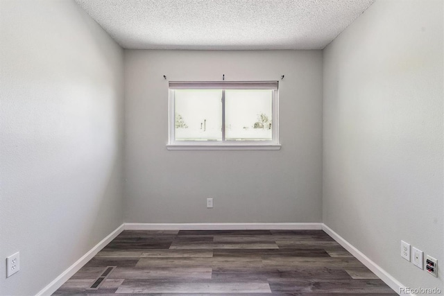 spare room with a textured ceiling, dark wood-type flooring, and baseboards