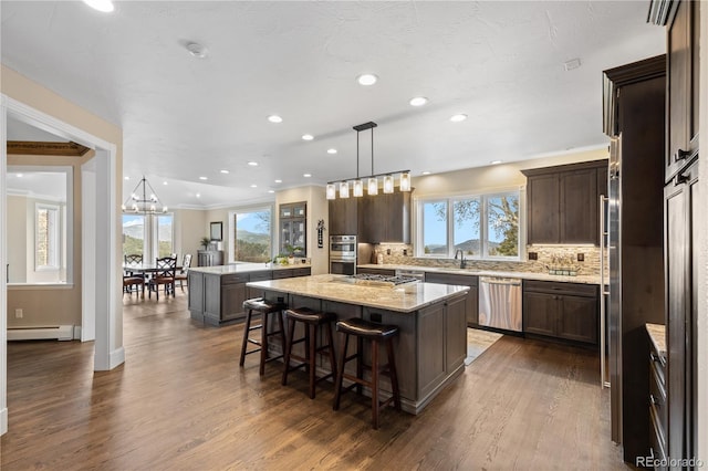 kitchen with a breakfast bar area, stainless steel appliances, a baseboard radiator, pendant lighting, and a center island